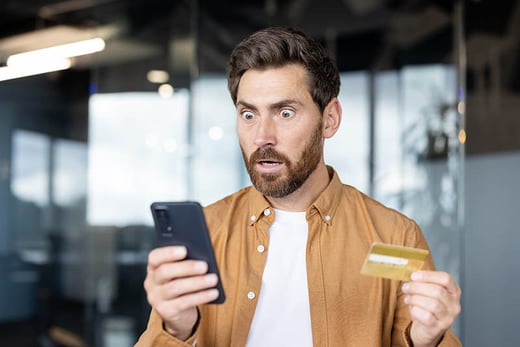 man looking shocked holding phone and credit card
